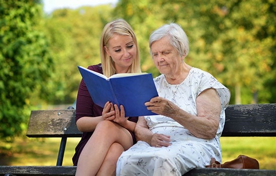 Young Woman Reading A Book Elderly Woman In The Park.
