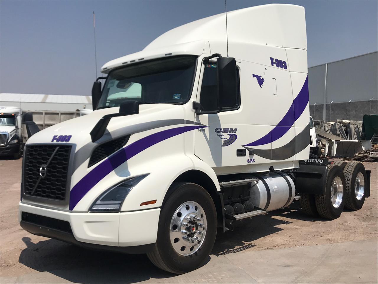 Camión Volvo blanco con detalles en azul y morado estacionado en un área abierta, visto de perfil.