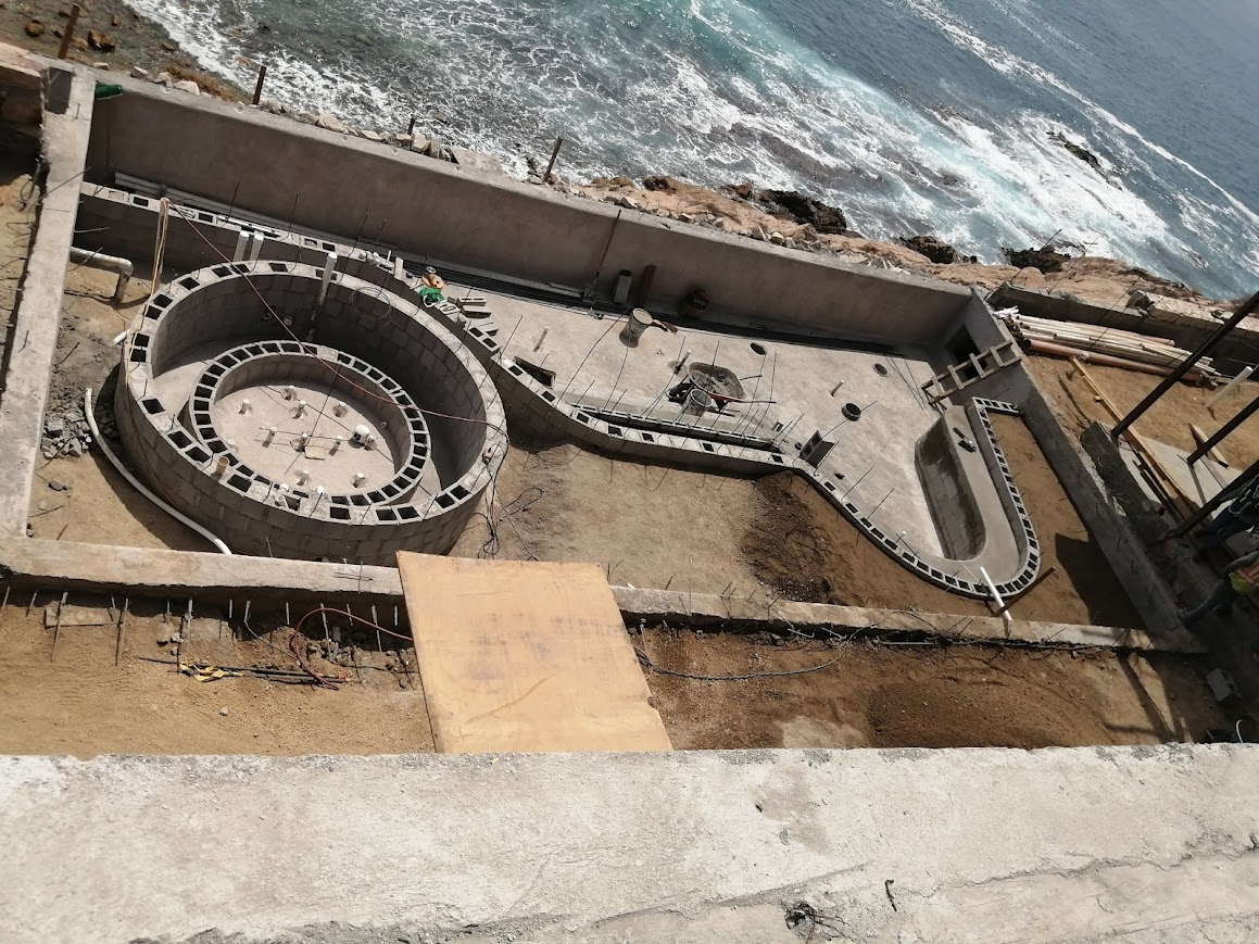 Construcción de casa moderna en la playa con cielo despejado, palmeras, y trabajadores en acción.