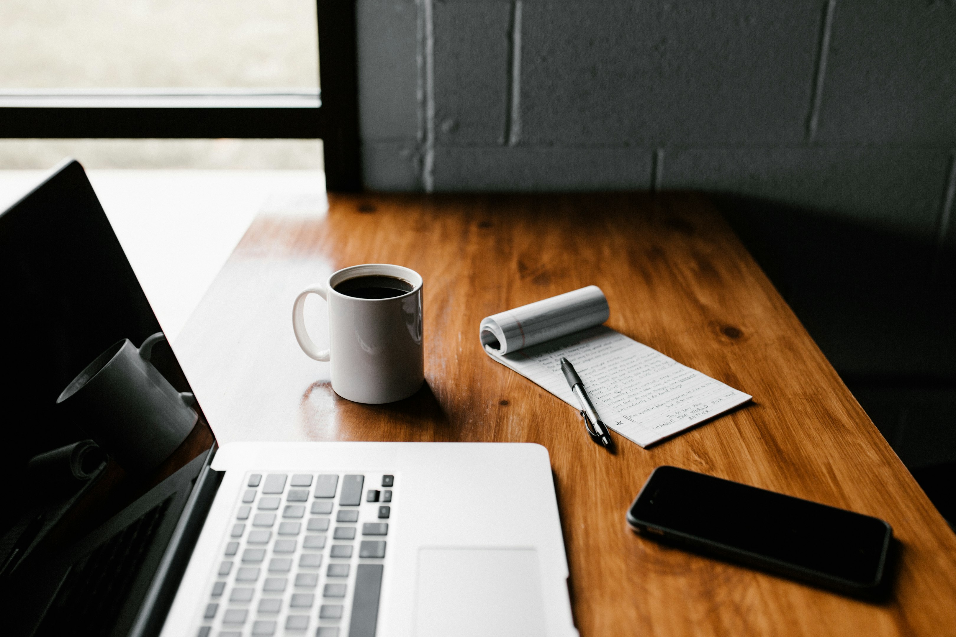 MacBook Pro, taza de cerámica blanca y teléfono inteligente negro en la mesa