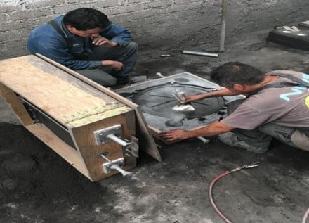 Dos personas trabajando en la creación de moldes de arena para piezas de fundición, utilizando herramientas manuales en un taller con suelo de cemento.