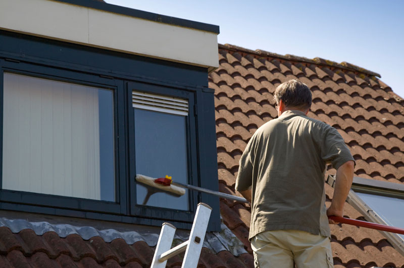 Man on a roof washing a window