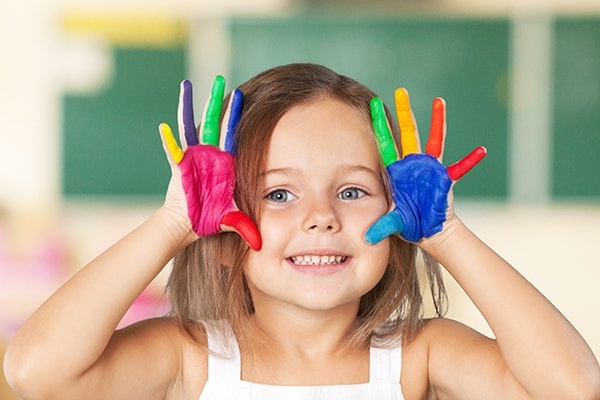 Cute Smiling Little Girl with Hands in Paint