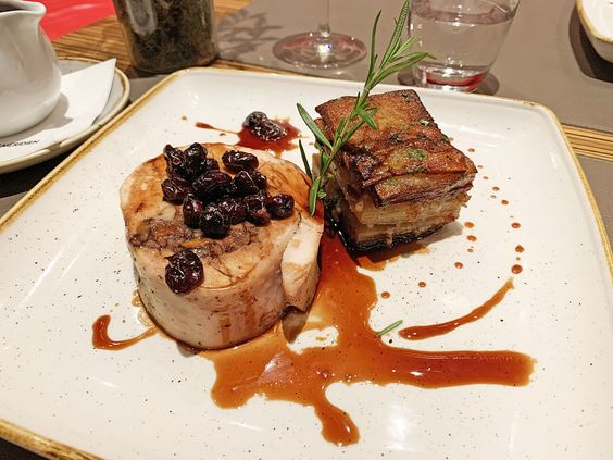 Plato gourmet con carne de cerdo asada con salsa y guarnición de papas, decorado con romero fresco.