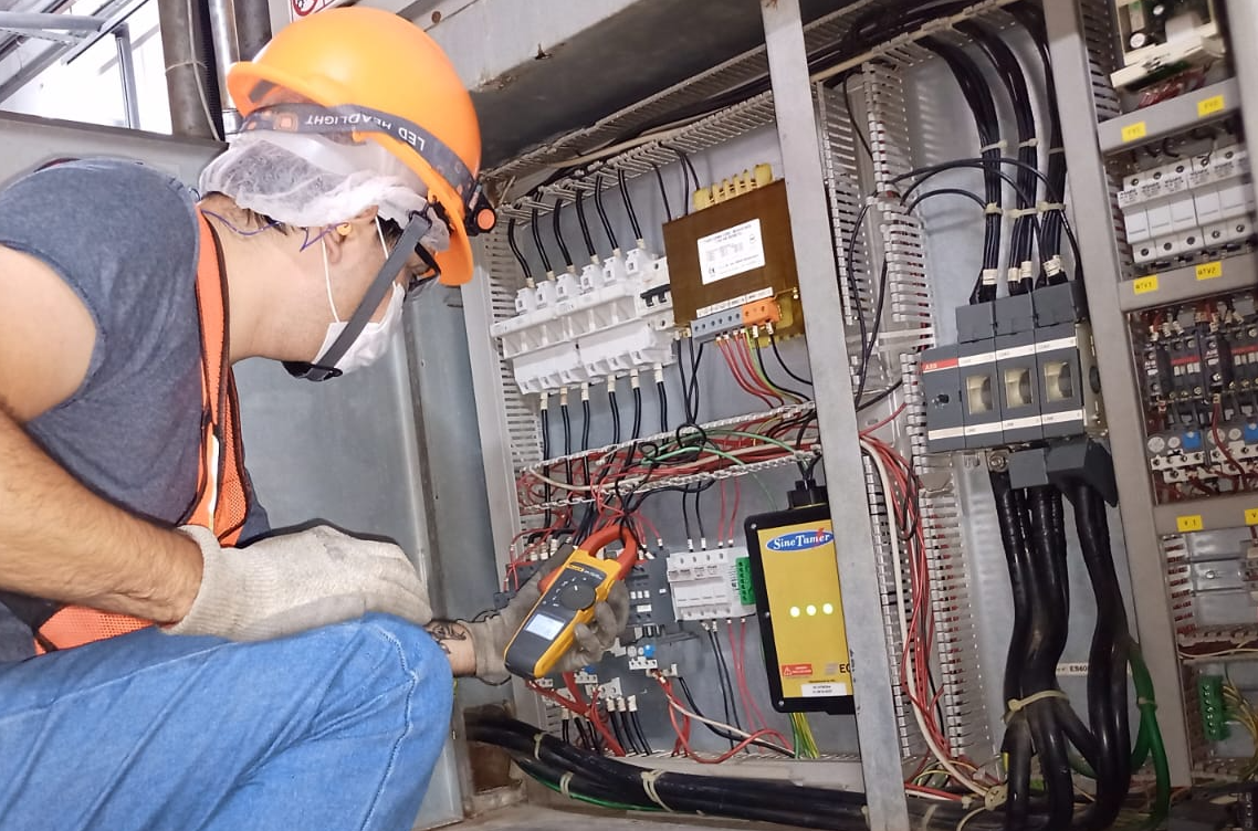 Técnico con casco y guantes trabajando en un panel eléctrico utilizando un multímetro.