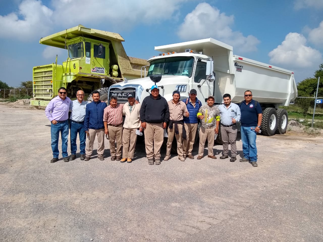 Grupo de hombres frente a camiones de construcción en un sitio de trabajo bajo un cielo parcialmente nublado. Grupo de hombres frente a camiones de construcción en un sitio de trabajo bajo un cielo parcialmente nublado.