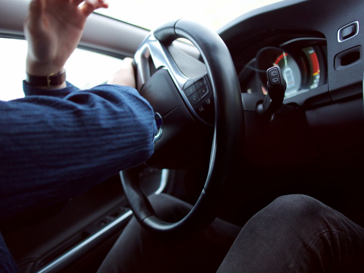 Man with hand on steering wheel driving a car
