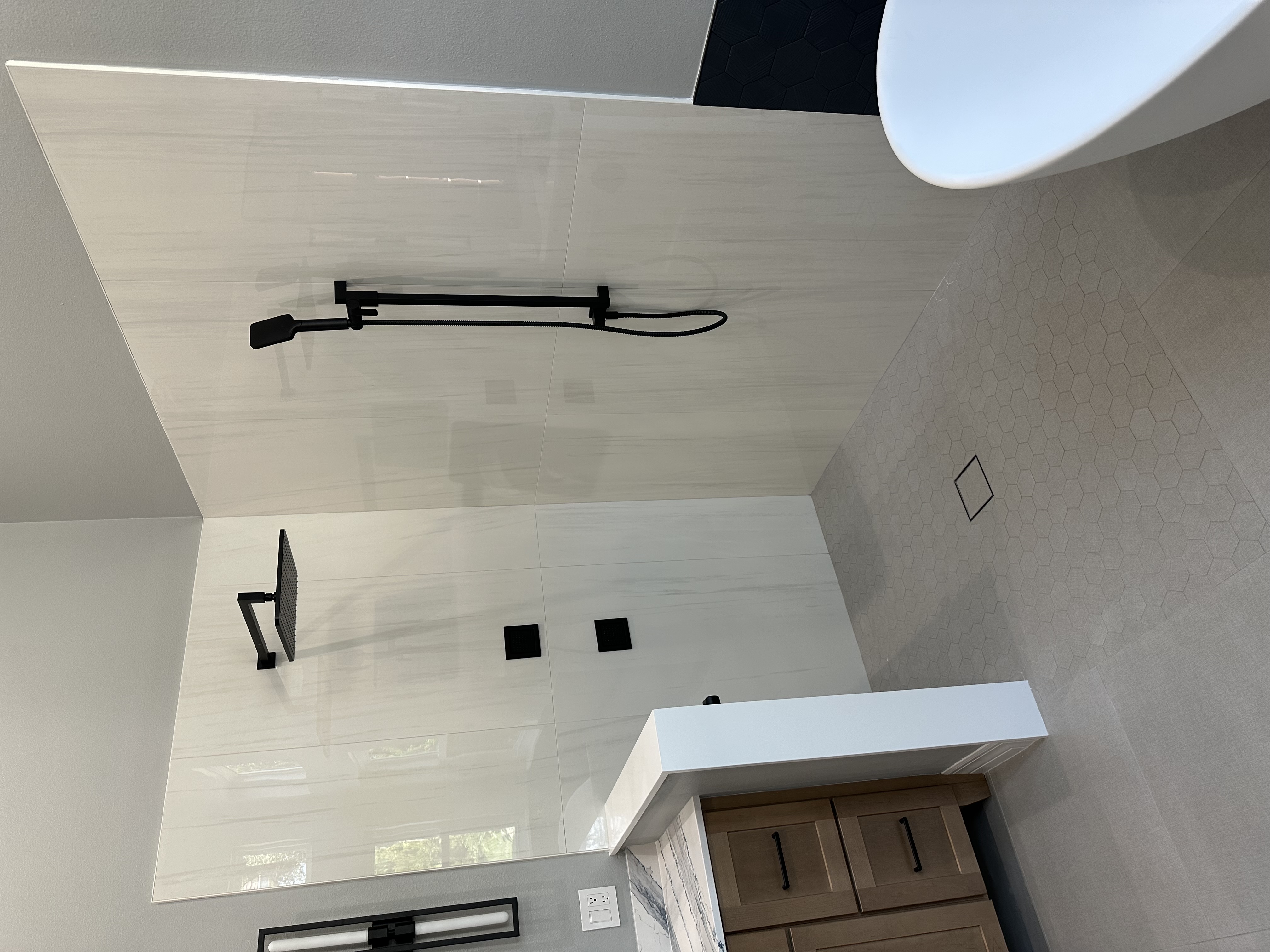 A spacious walk-in shower with large-format wall tile, a stylish hexagon shower floor, and matte black fixtures adds a clean, modern touch to the space.