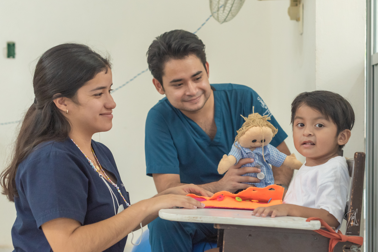 Dos profesionales de la salud, uno sonriendo y otro escribiendo, en un entorno de oficina moderna con plantas y luz natural. Dos profesionales de la salud, uno sonriendo y otro escribiendo, en un entorno de oficina moderna con plantas y luz natural.