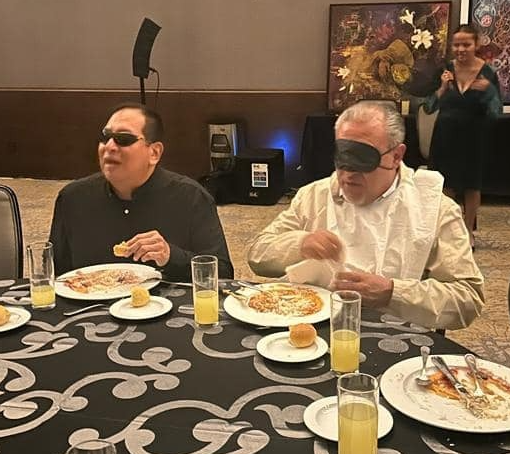 Hombre con traje y corbata roja frente a una bandera de México en un entorno urbano.