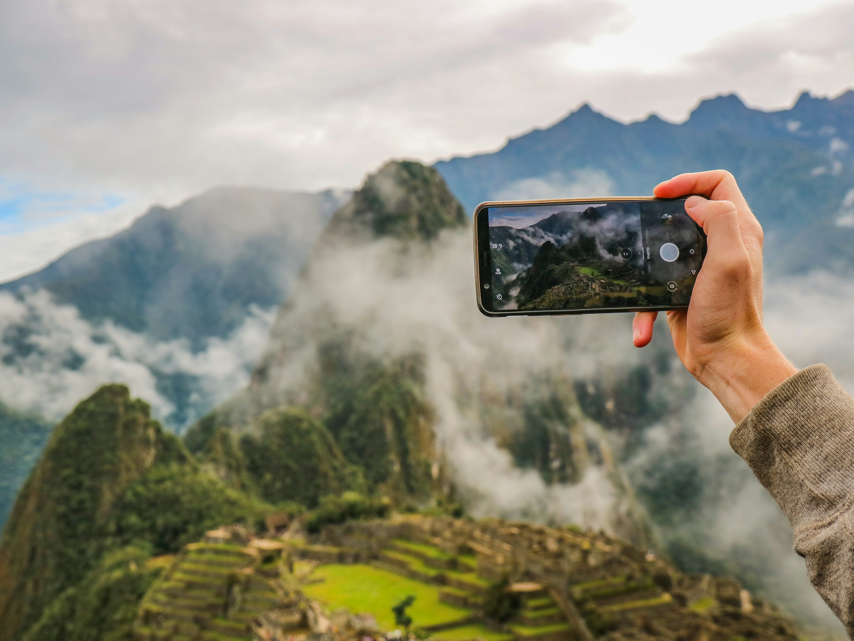 persona sosteniendo smartphone tomando foto de montaña verde