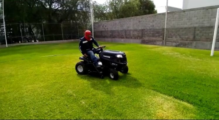 Persona montando un tractor cortacésped en un jardín bien cuidado. Persona montando un tractor cortacésped en un jardín bien cuidado.