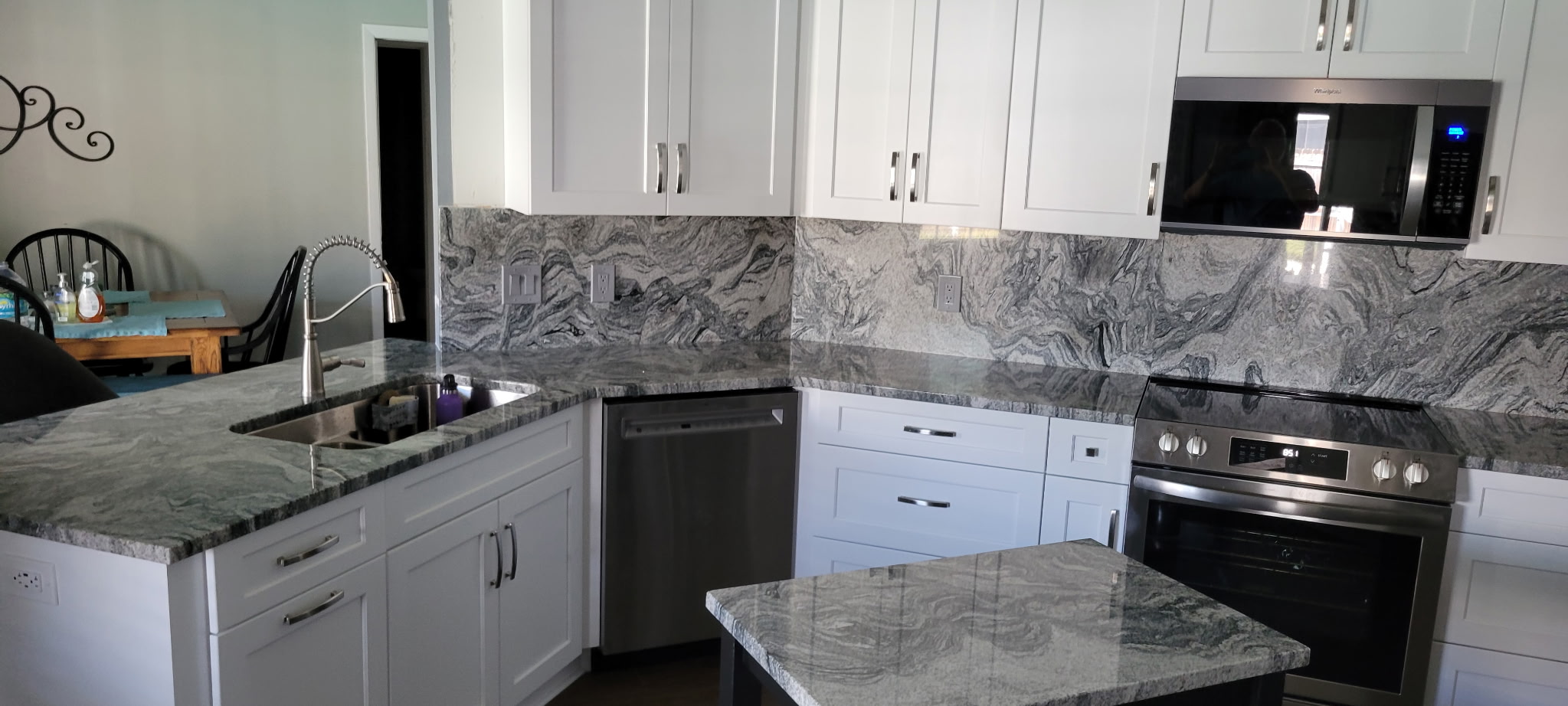 Stunning kitchen with semi-custom painted Sea Salt cabinetry, satin nickel hardware, and rich granite countertops with a matching full granite backsplash.