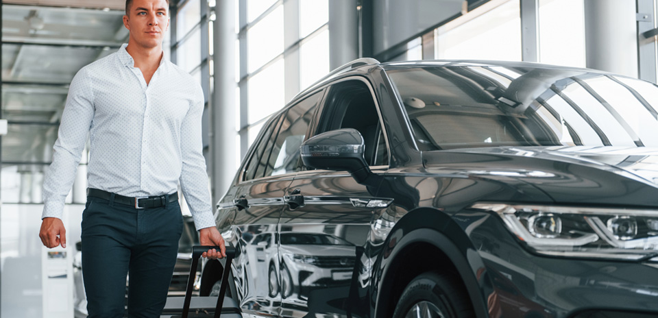 Business traveler in suit walking with suitcase near rideshare