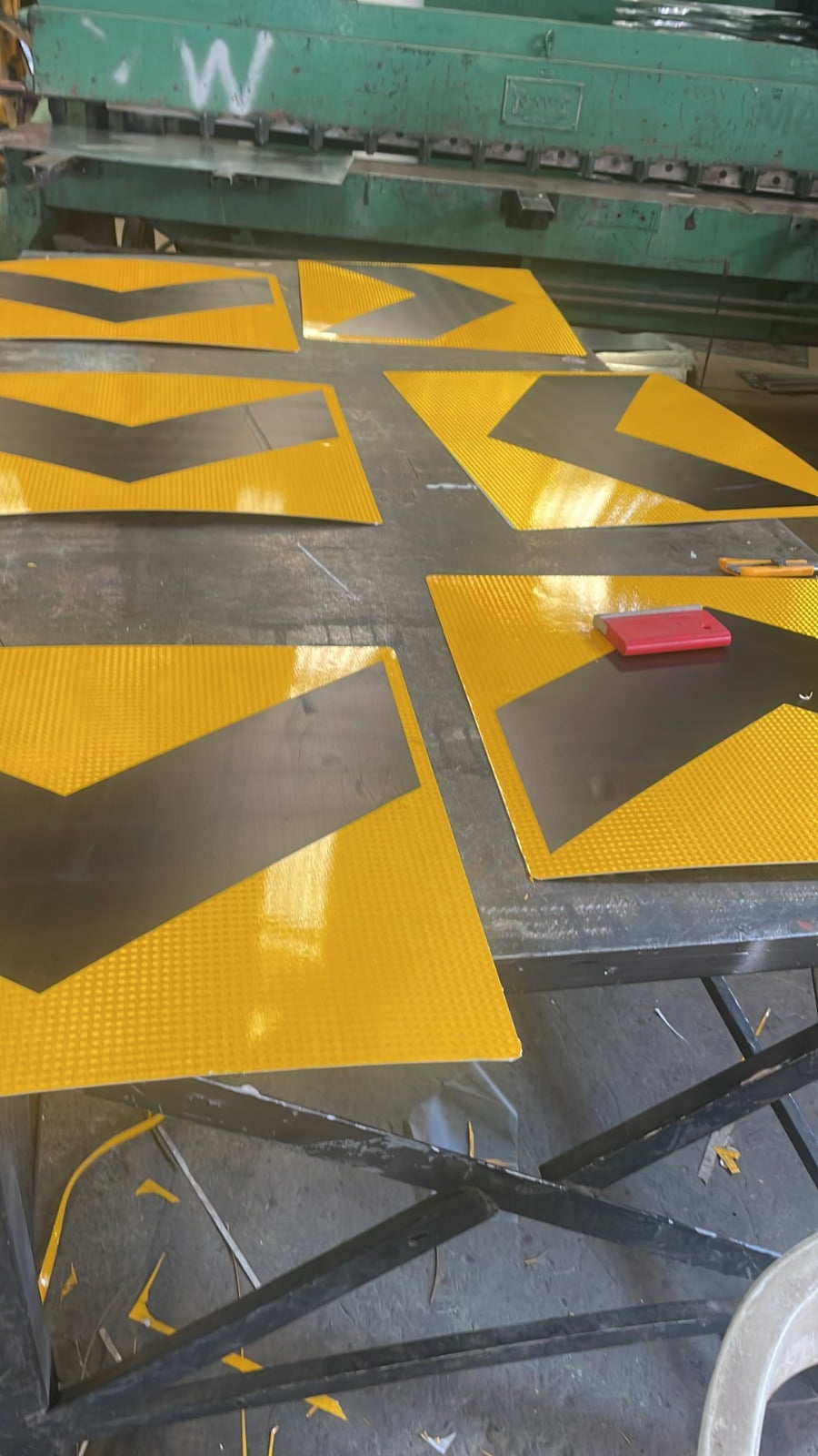 Señales de tráfico reflectantes amarillas con flechas negras en proceso de fabricación en una máquina verde.