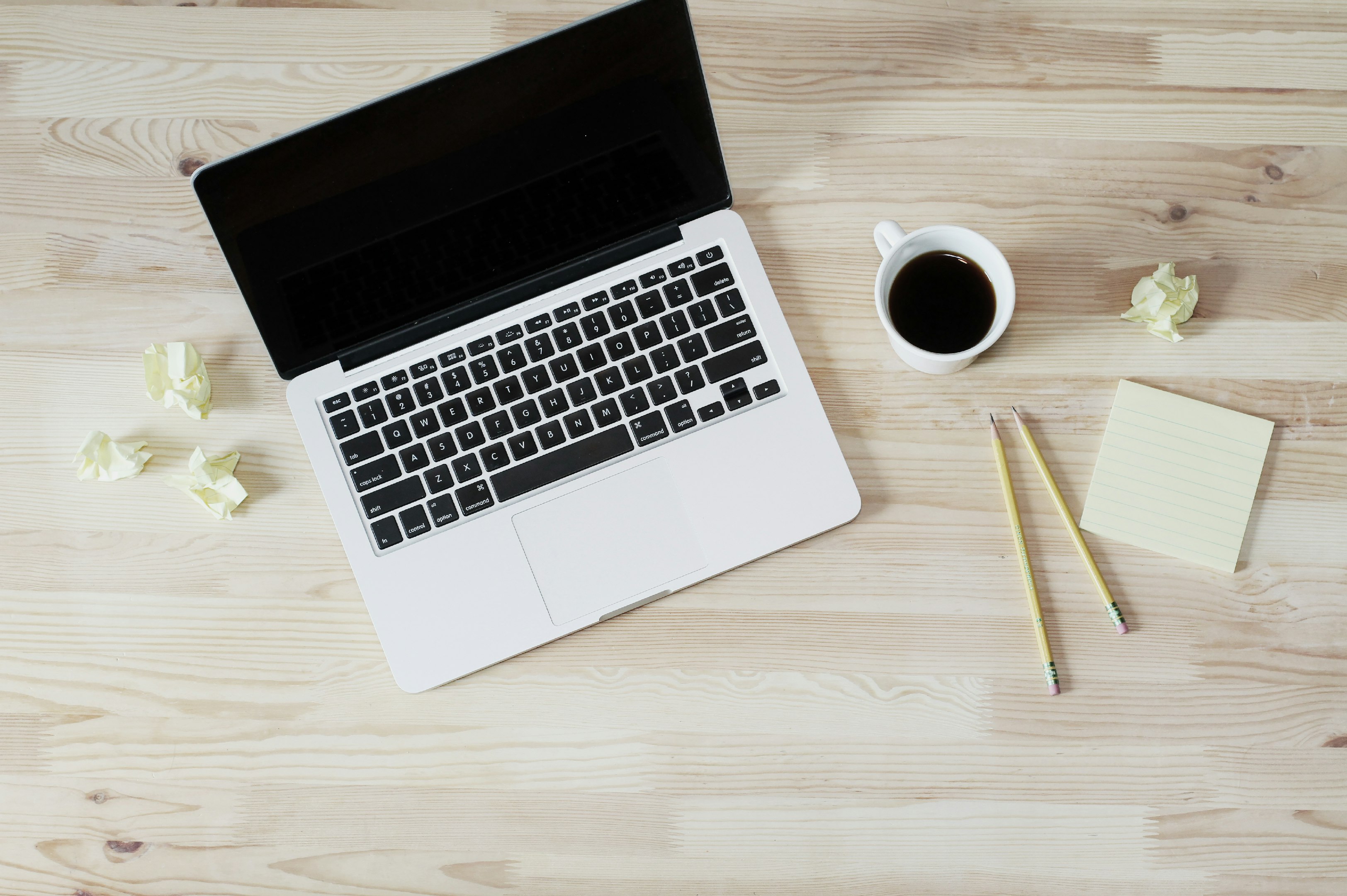 MacBook Pro apagado junto a una taza de cerámica blanca llena de café
