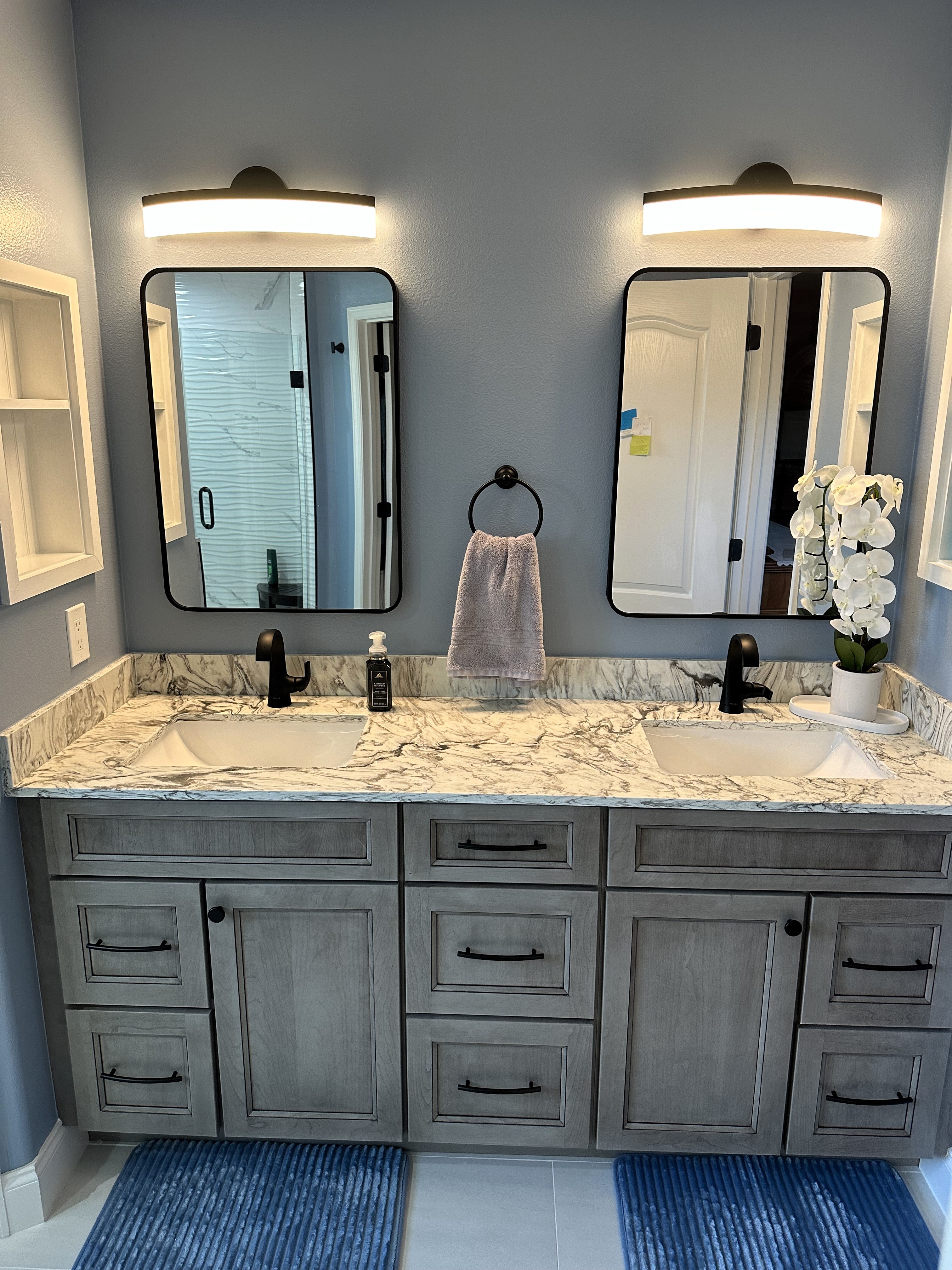Calm and serene primary bathroom featuring semi-custom cherry-stained Peppercorn cabinetry, matte black knobs/handles, and Pompeii Avalanche quartz countertop with matching 4" backsplash.
