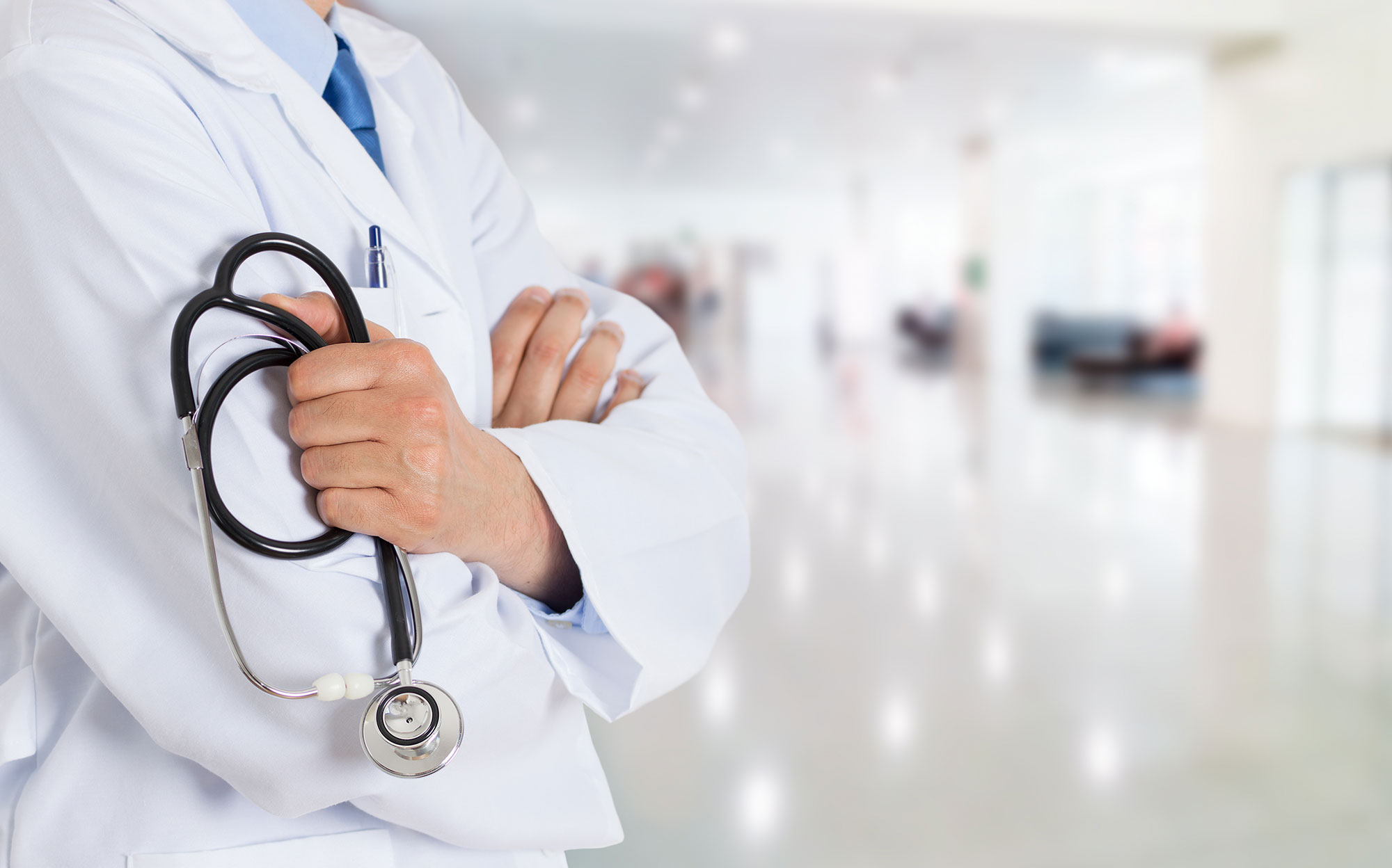 Doctor con bata blanca sosteniendo un estetoscopio en el pasillo de un hospital.