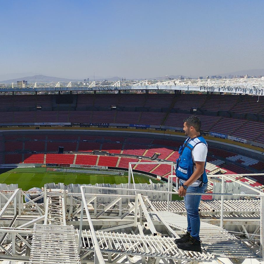 Hombre trabajando en una plataforma elevadora junto a un edificio industrial bajo un cielo azul.