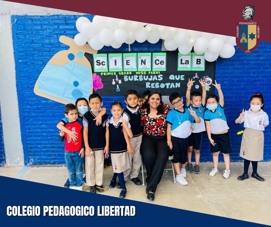 Estudiantes sonrientes en un aula, con cuadernos y bolígrafos sobre la mesa, enfoque en un hombre y una mujer con gafas.