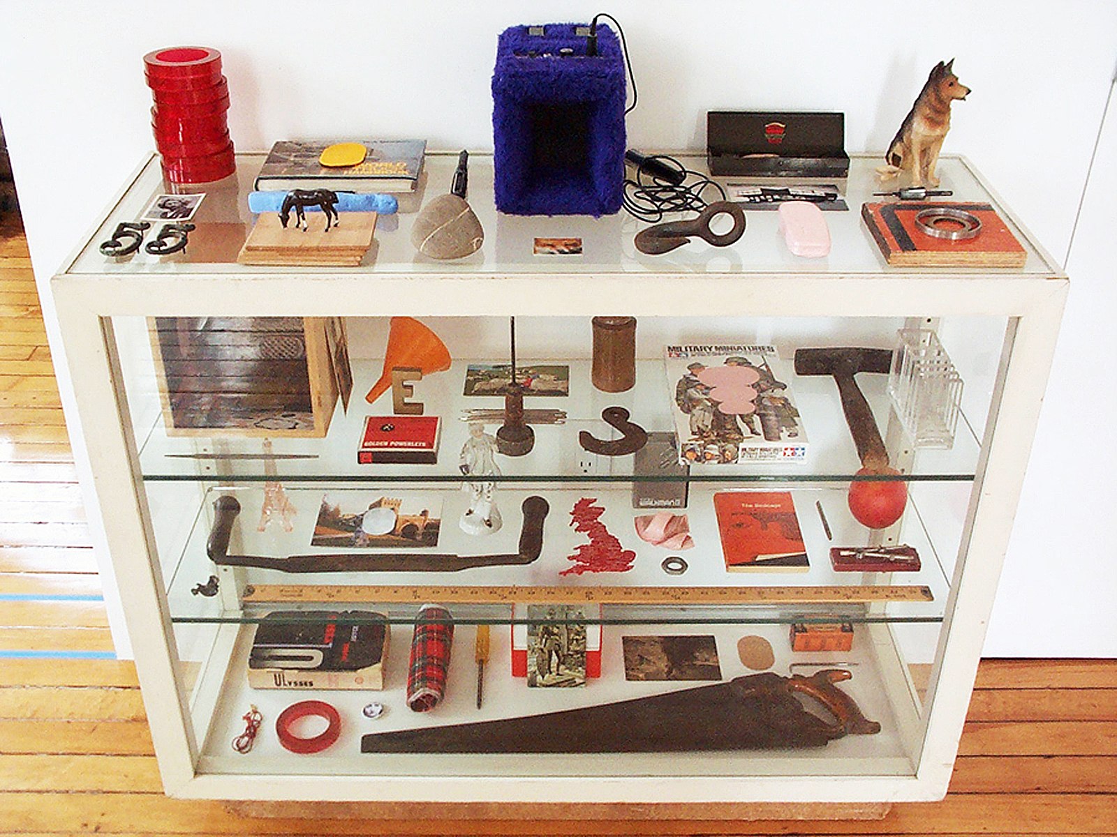 A white display case full of objects including saws, postcards and a dog figurine.