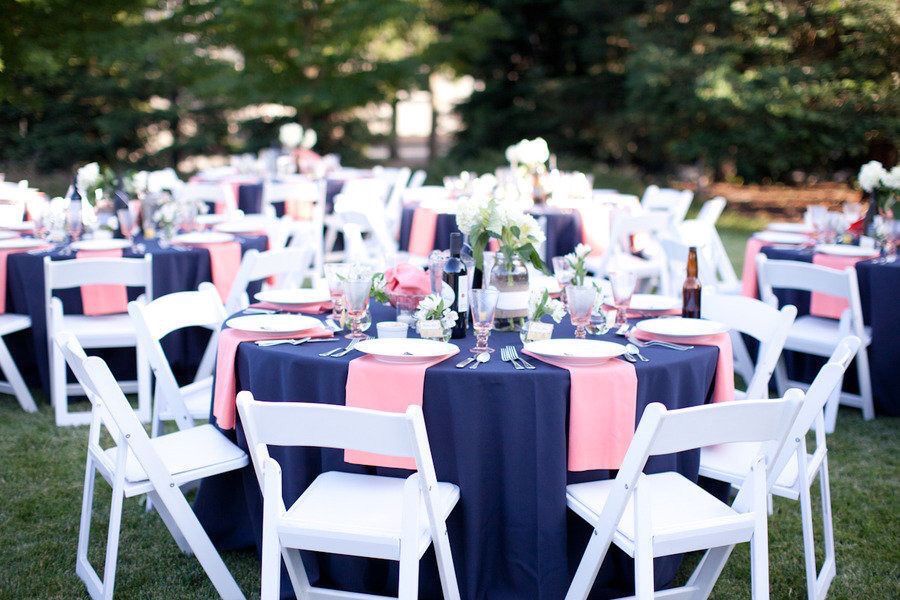 Mesas de banquete al aire libre decoradas con manteles azules y rosados, sillas blancas, y arreglos florales, en un entorno verde. Mesas de banquete al aire libre decoradas con manteles azules y rosados, sillas blancas, y arreglos florales, en un entorno verde.