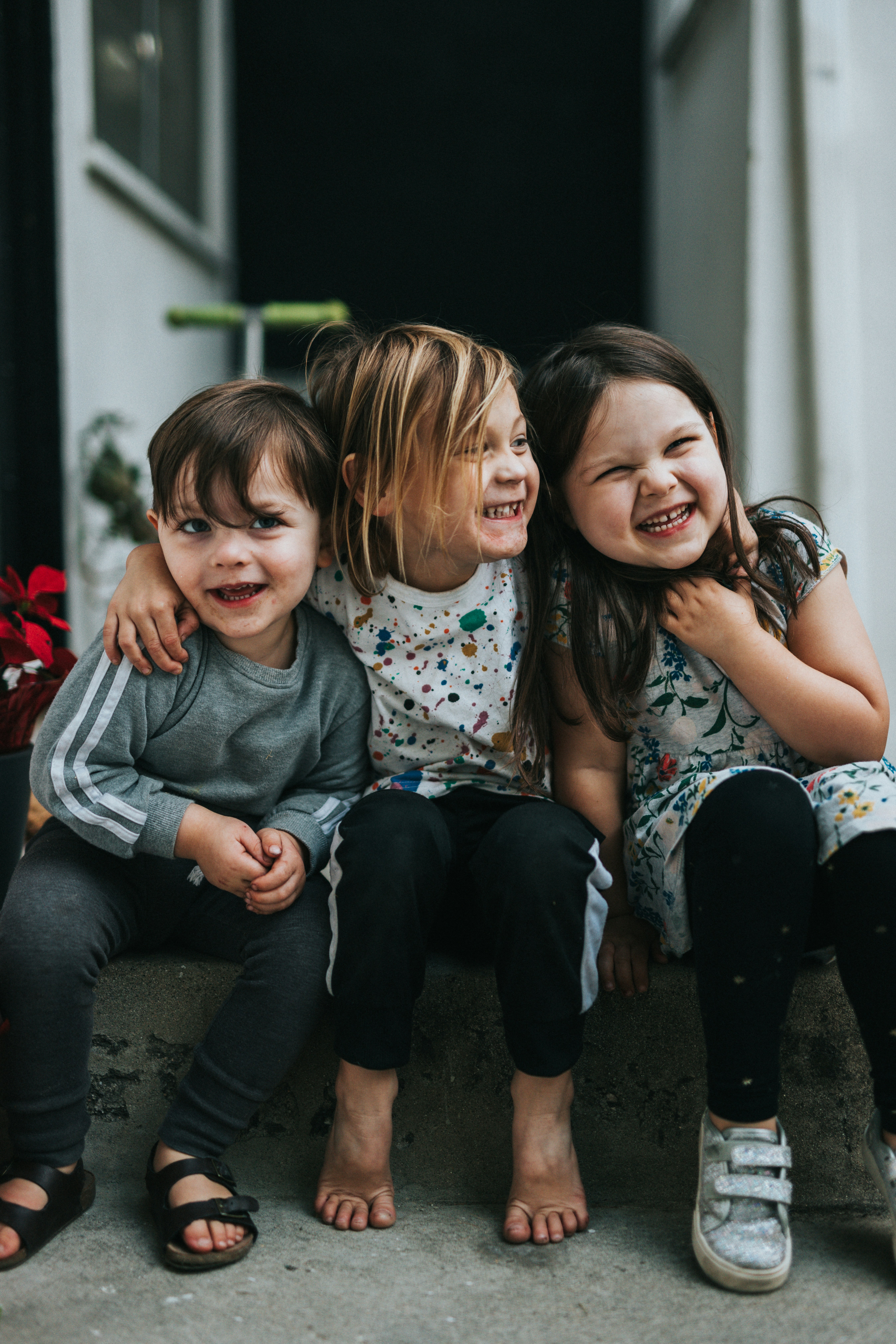 Tres niños pequeños felices sonriendo y abrazados sentados en un escalón al aire libre