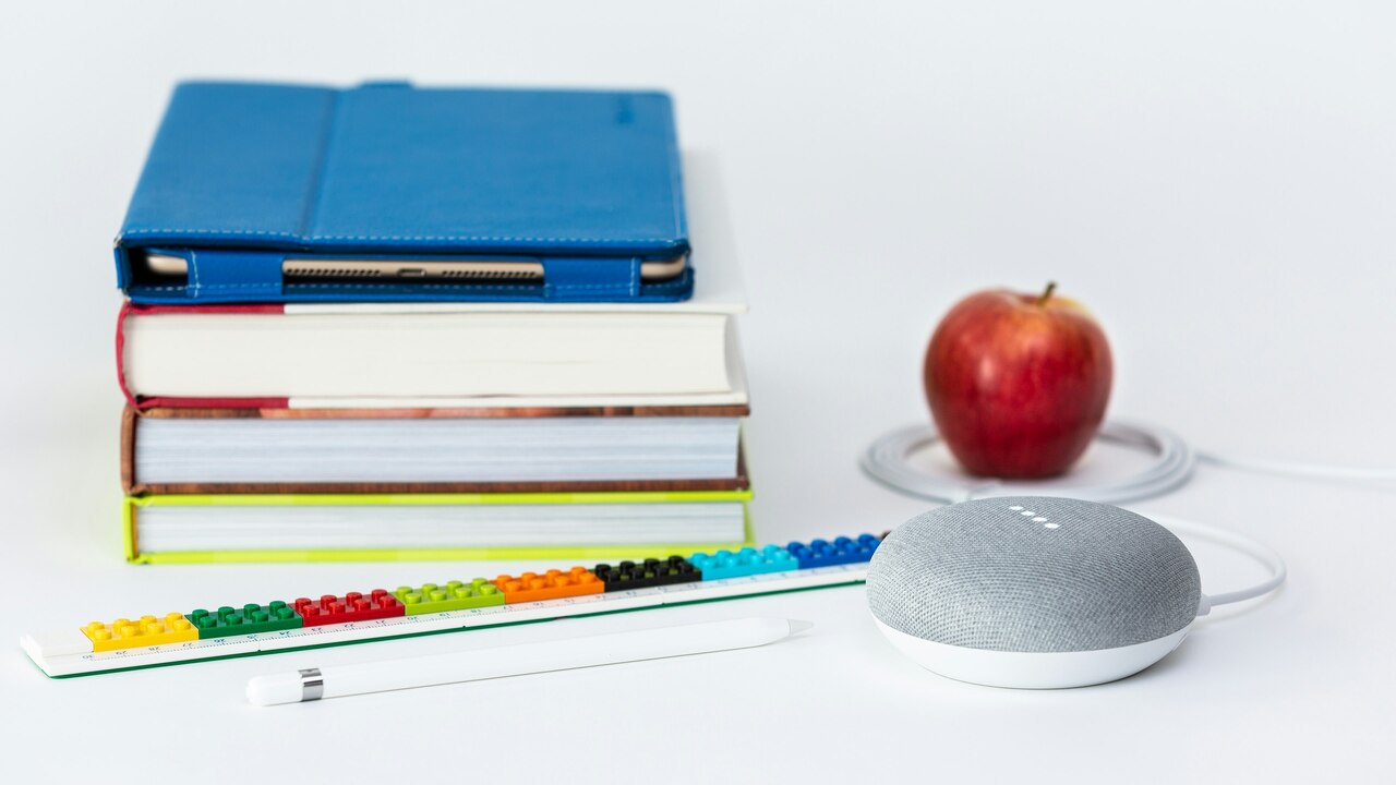 manzana honeycrisp cerca de libros y altavoz inteligente Google Home Mini de tiza