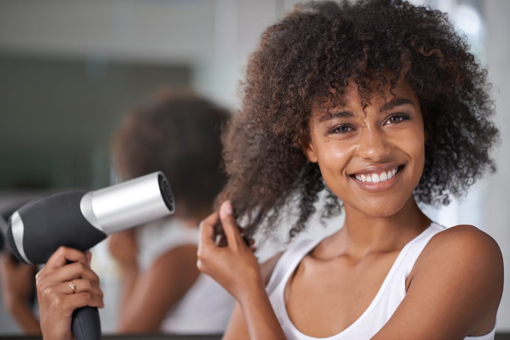 An African American woman blow drying her hair