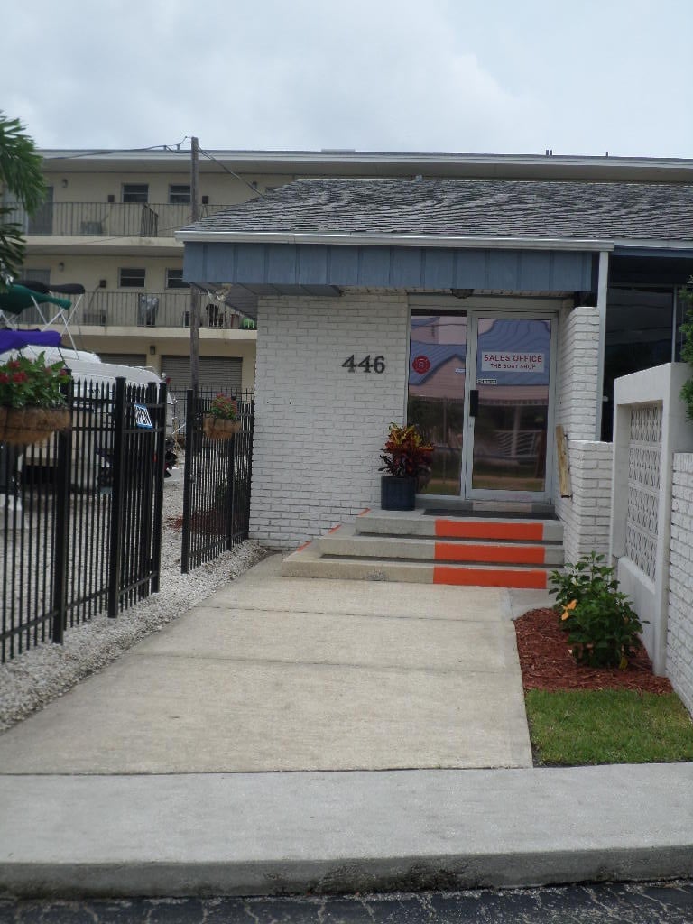 Apartment sales office entrance at 446 with white brick exterior, gated walkway, stairs, and landscaping