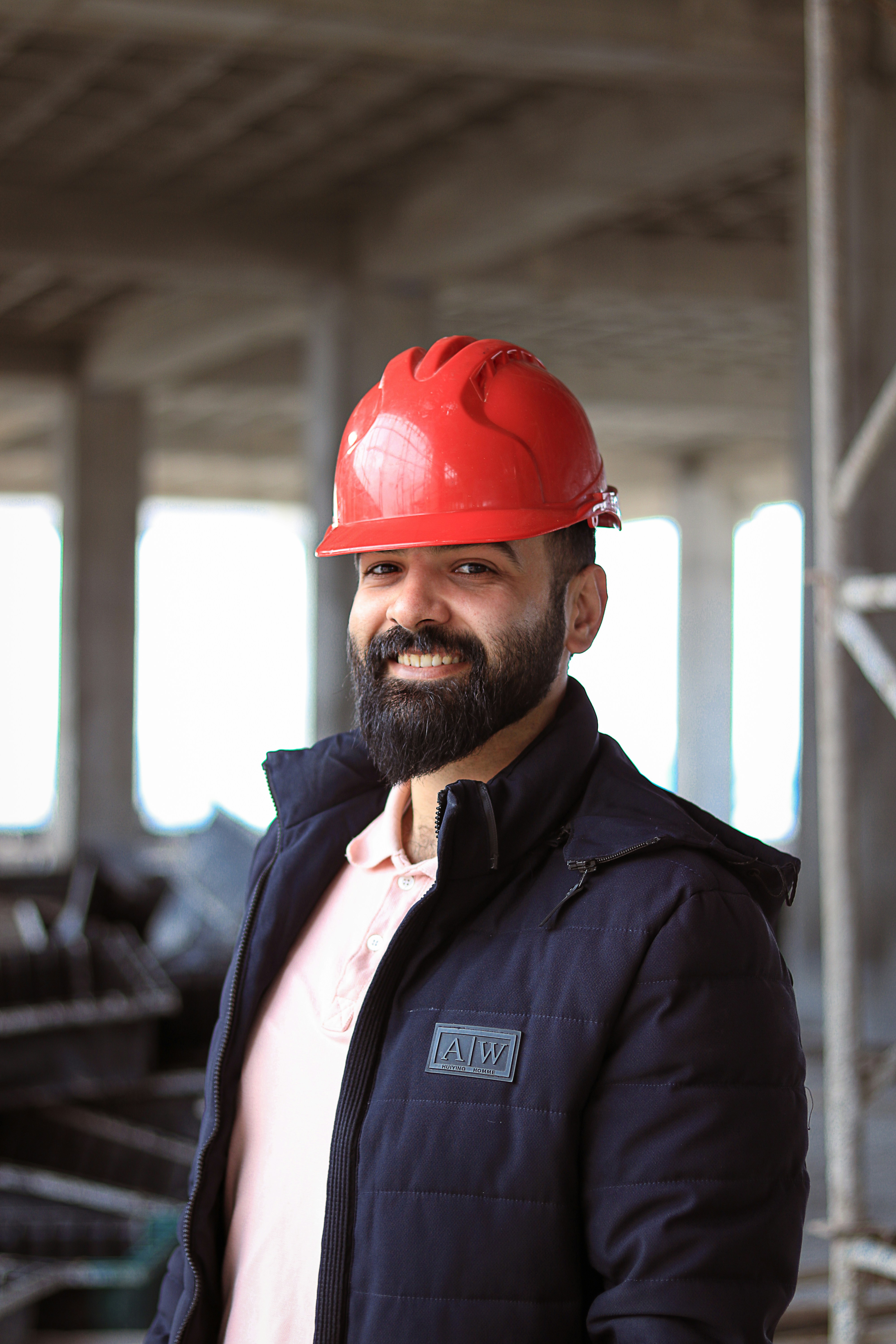 Construction worker in a yellow hard hat and sunglasses smiling at a construction site.