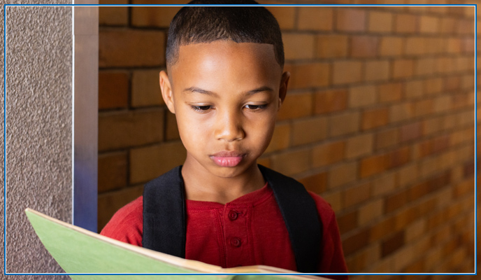 Boy standing in a hallway reading a notebook.