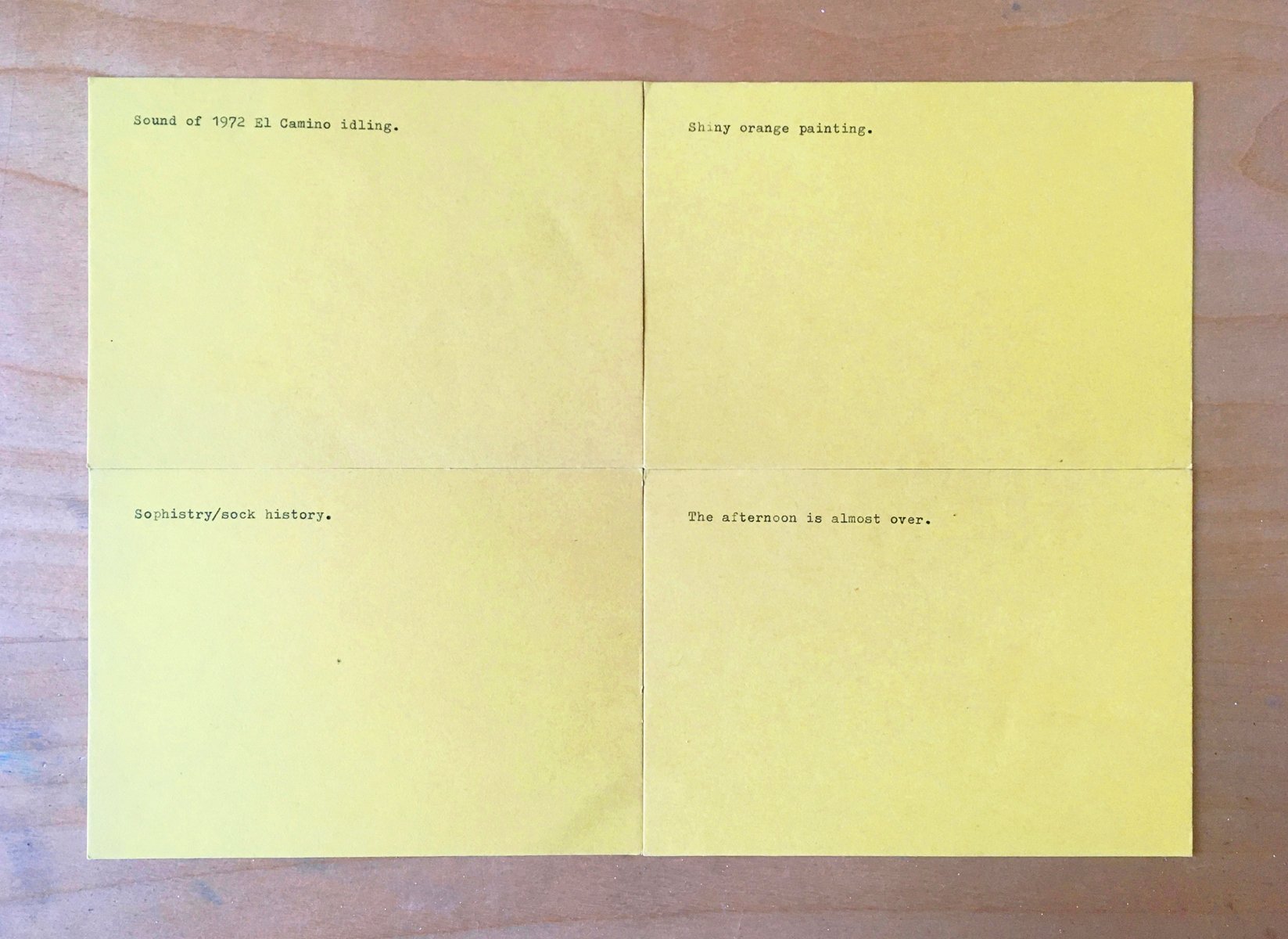 Four yellow index cards, one line is typed on each, placed on a plywood table.