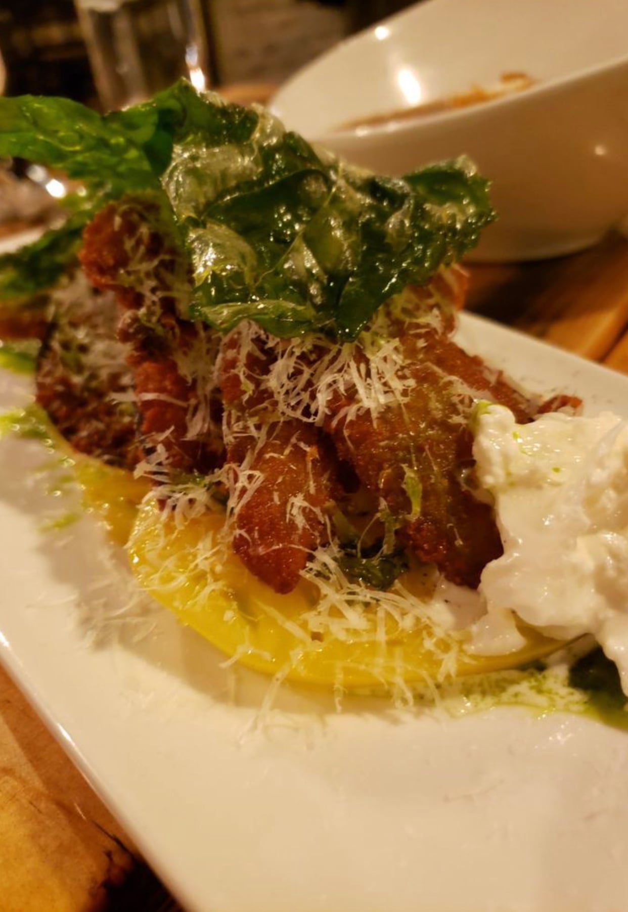 Close-up of crispy fried dish with cheese, greens, and creamy topping on a white plate.