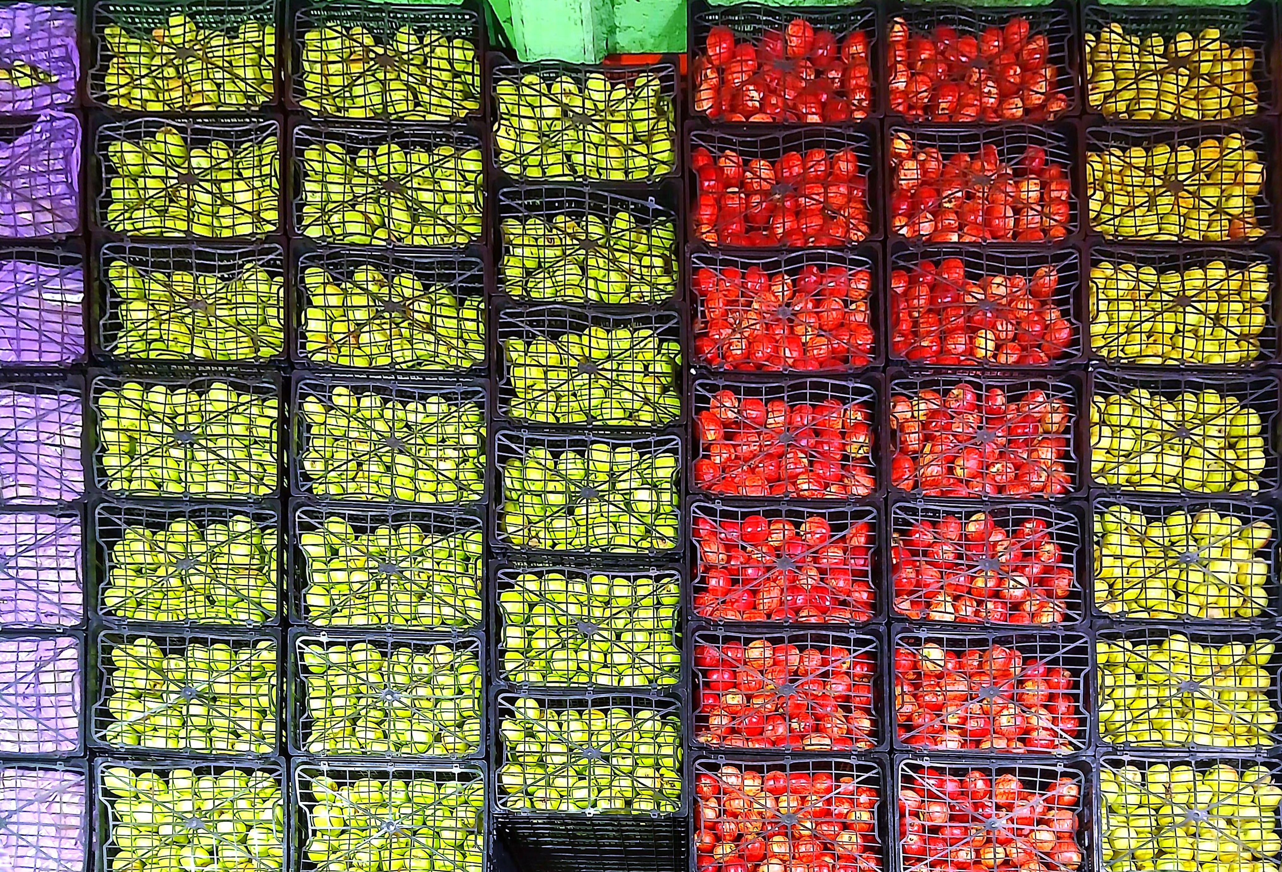 Cajas apiladas con pimientos morados, amarillos y rojos en un mercado.