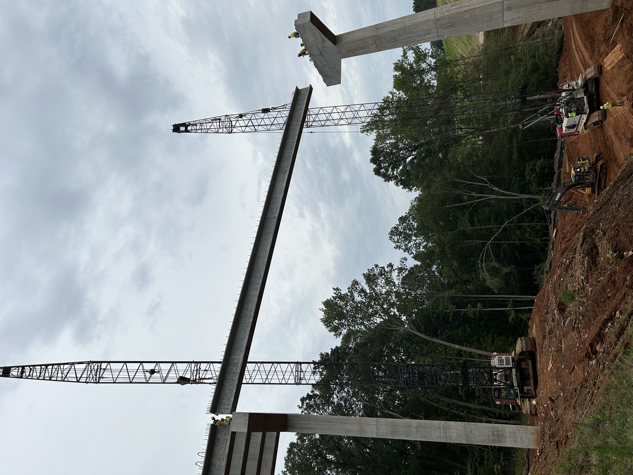 Highway overpass construction site with cranes, excavator, cement trucks, workers, and traffic on a modern urban road Highway overpass construction site with cranes, excavator, cement trucks, workers, and traffic on a modern urban road