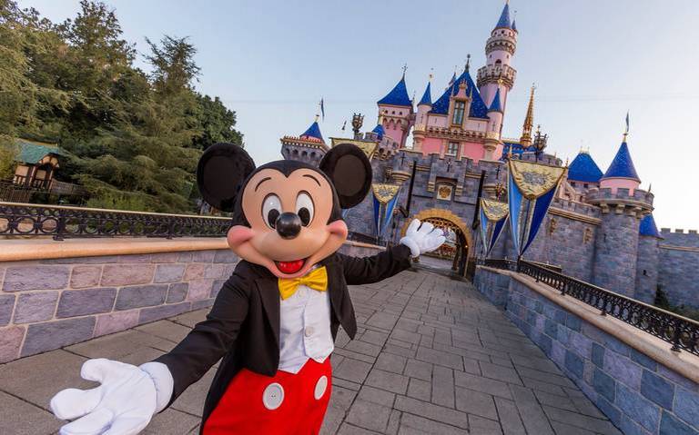 Mickey Mouse frente al castillo de Disneyland con cielo despejado.