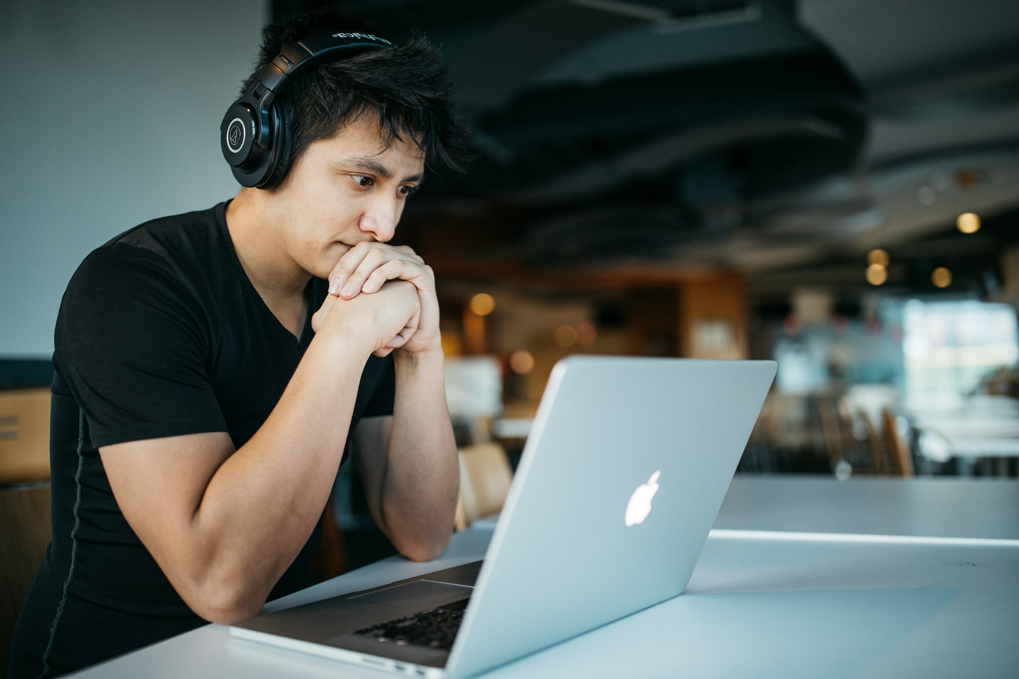 Focused person wearing headphones working on a laptop in a modern setting.