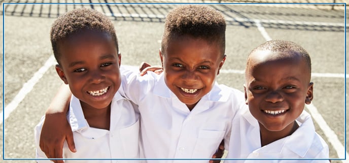 Three schoolboys smiling into the camera with white school shirts on