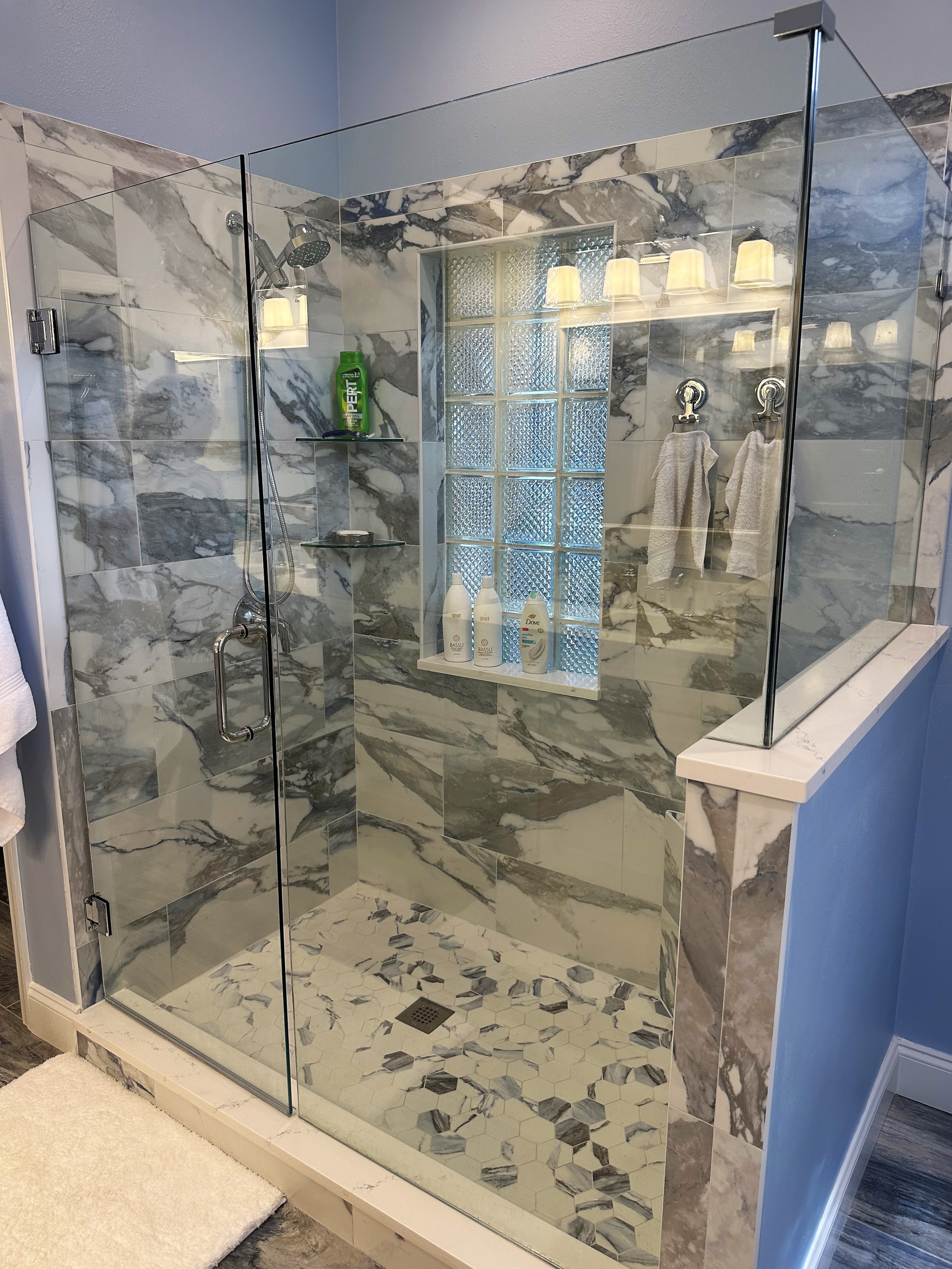 Beautiful and bright shower featuring Crash Blue tile and glass corner shelves for extra shower items. 