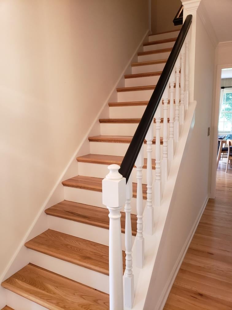 Elegant wooden staircase with white balusters and a dark handrail in a well-lit hallway.