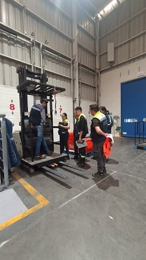 Personas en capacitación con equipo de carga en almacén industrial.