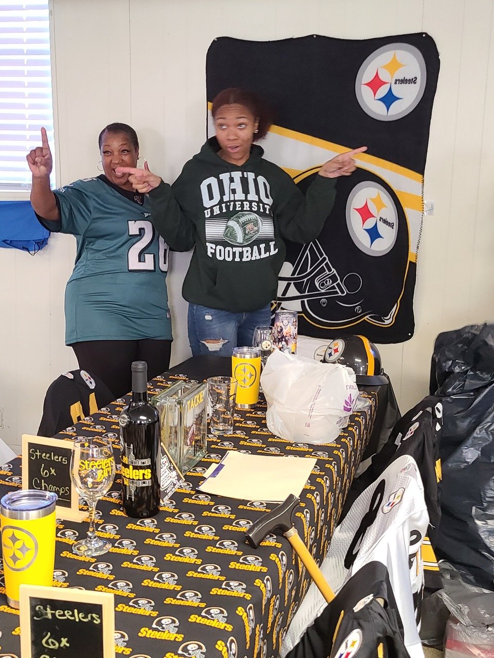 Two people posing in front of a Pittsburgh Steelers-themed table with branded merchandise, including cups, wine, and plaques, adorned with Steelers logos and decorations.