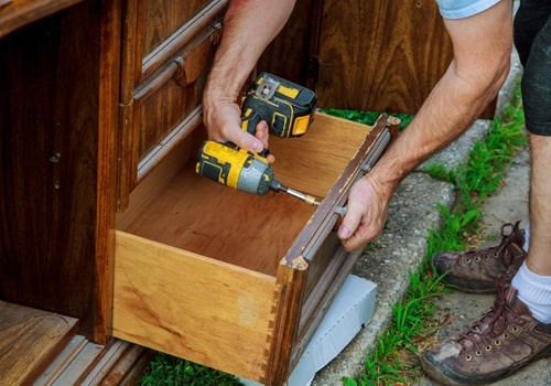 A Workman Fixing Cabinet With Screwdriver In Kitchen