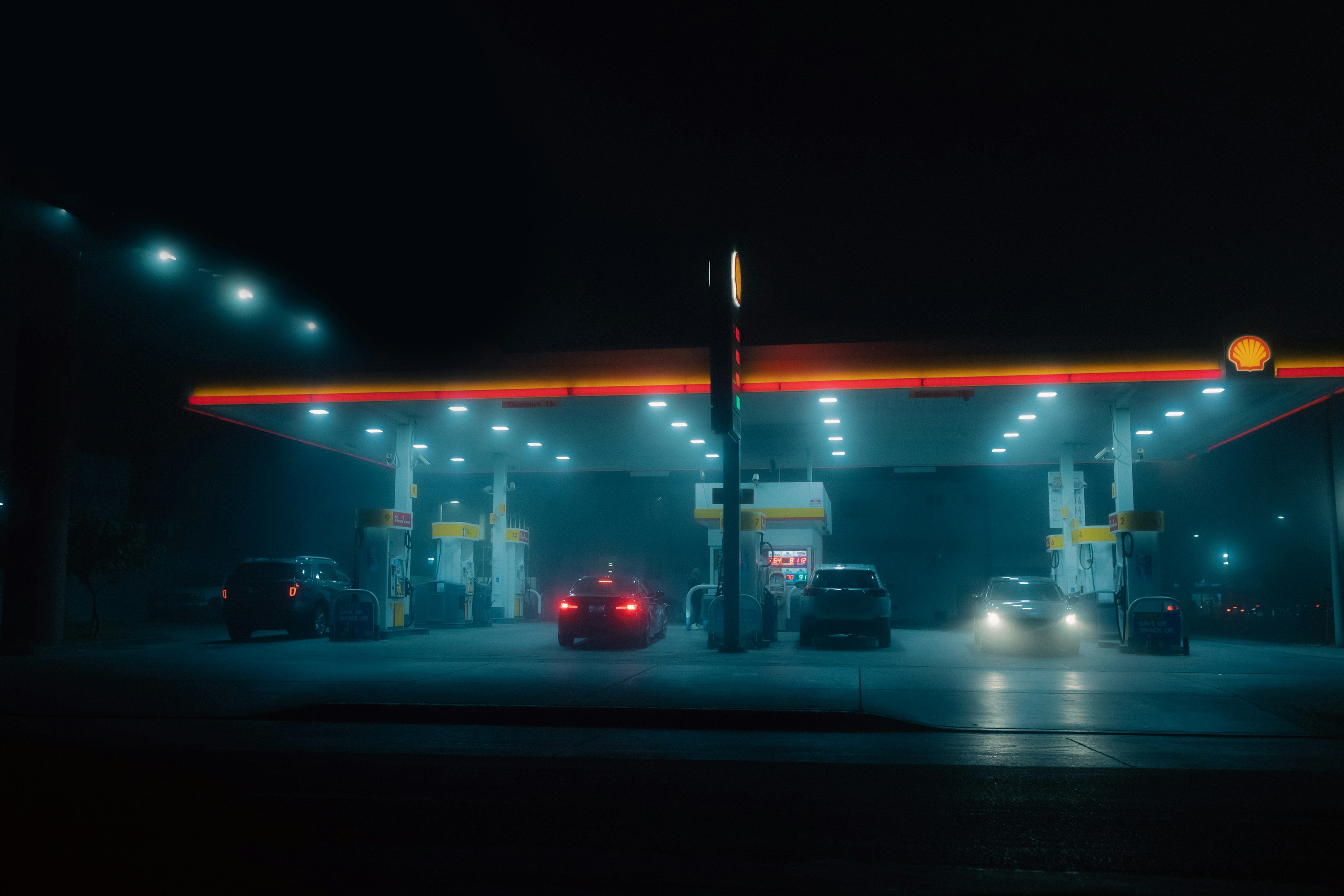 una estación de gasolina por la noche con coches estacionados en la bomba de gas