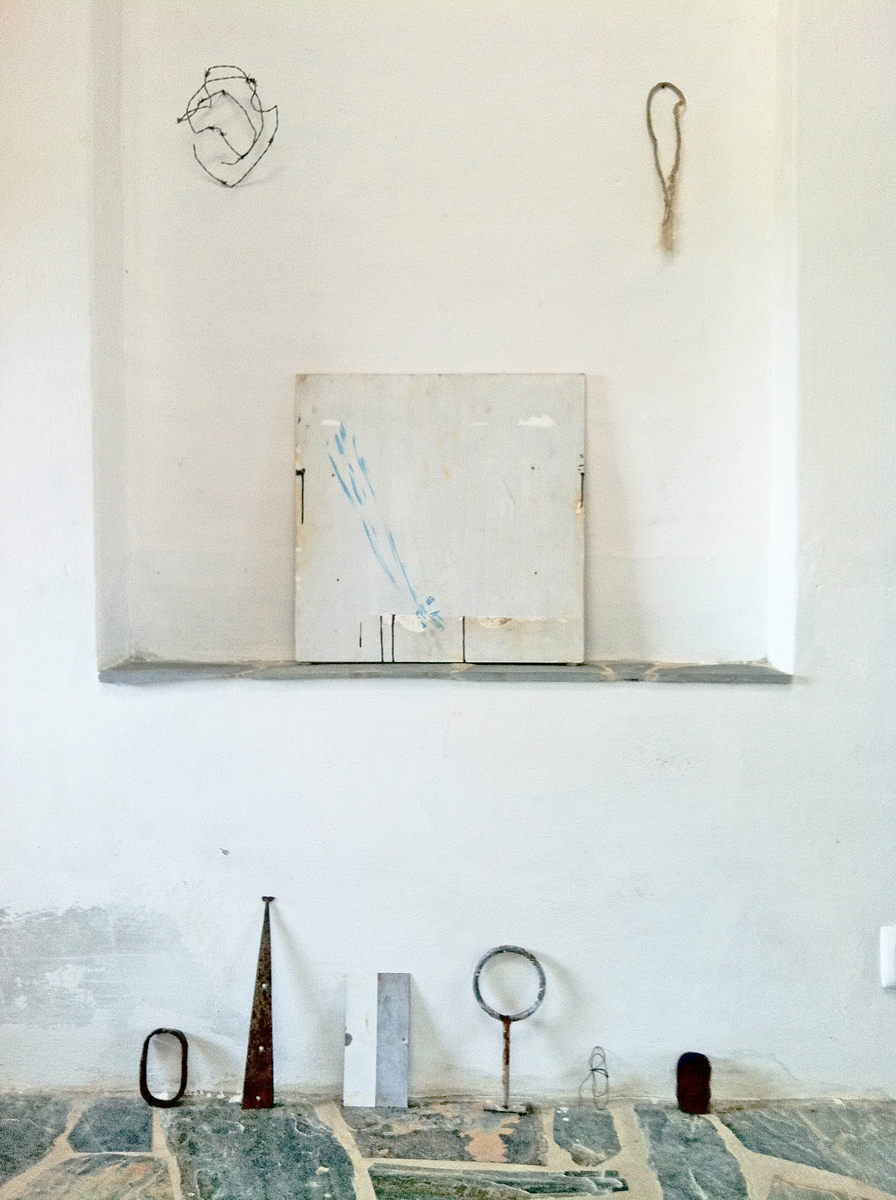 Rustic objects and a white painting in a whitewashed space with a stone floor.
