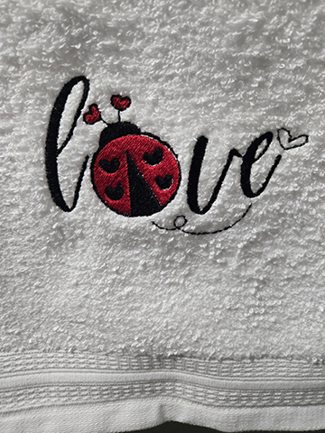 White hand towel with a ladybug and love embroidered on it
