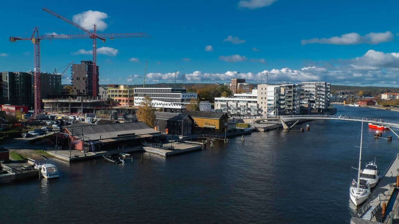 Modern buildings line a calm blue river with boats.