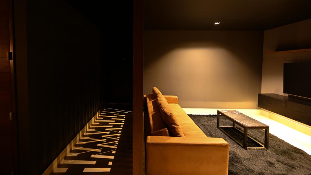 Interior moderno con sofá amarillo, pared oscura y mesa de centro en alfombra negra.