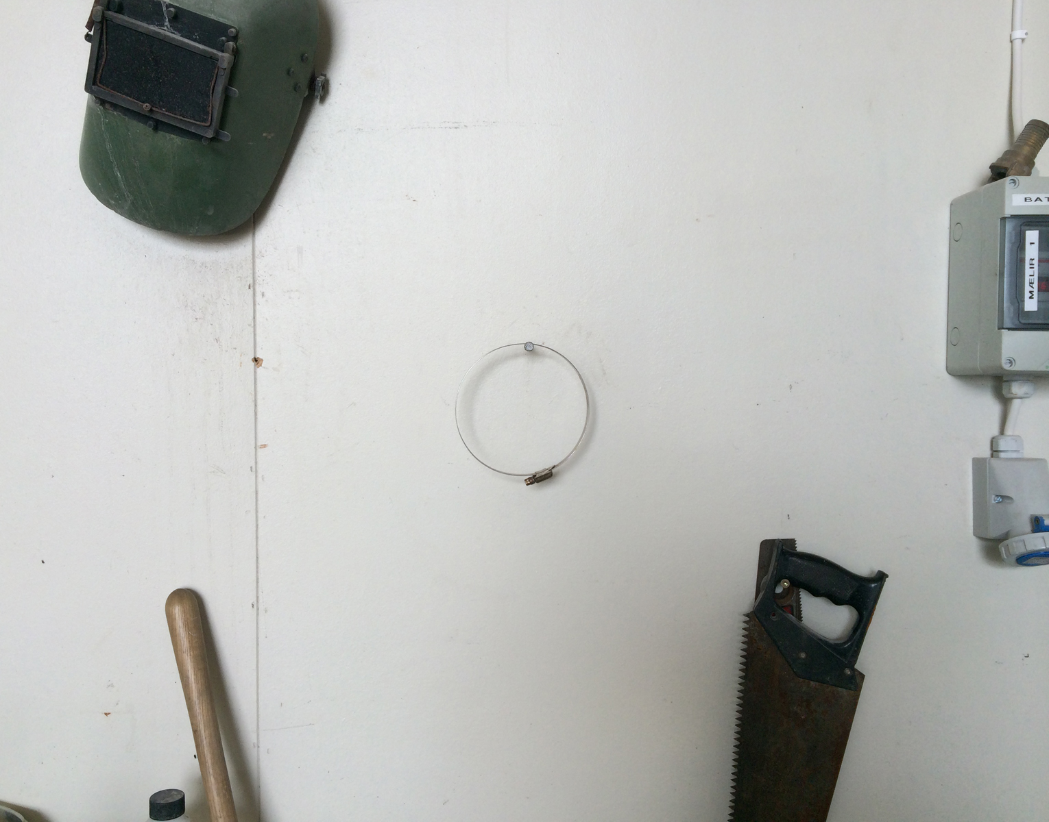 A welders mask, saw and centered circular pipe clamp hang on a white wall.